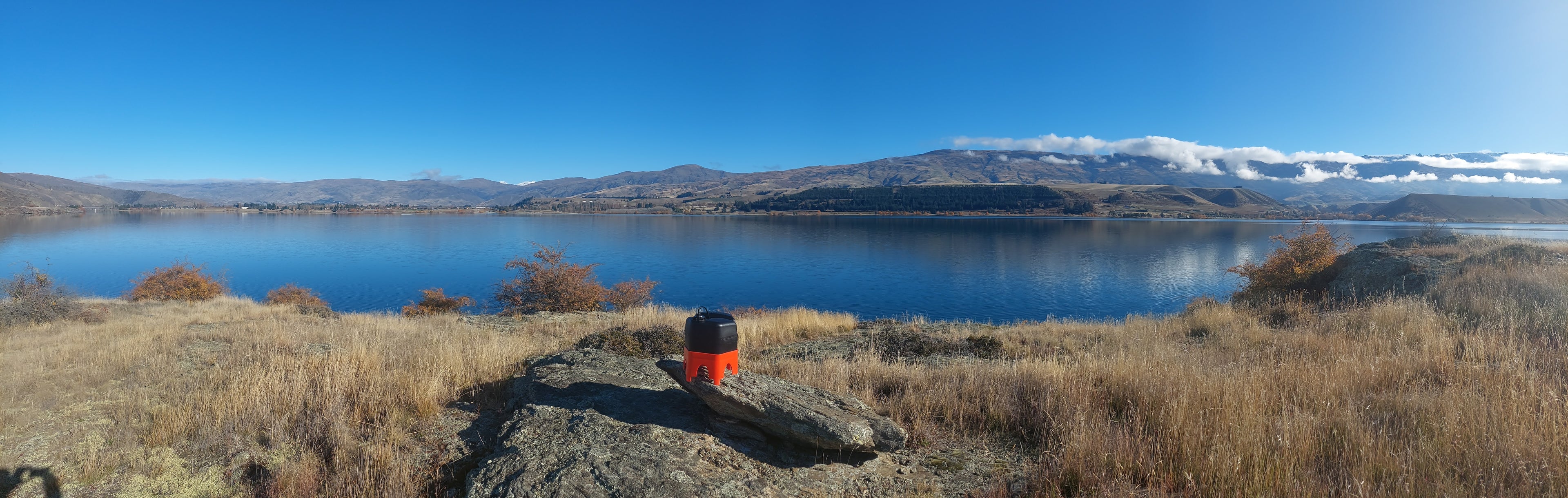 a h2ortigator pod in the foregound with an expansive beautiful view across lake dunstan looking towards cromwell with snow and cloud capped mountain ranges in the distance